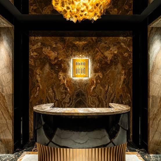 The Harbour Sixty host stand — onyx and brass, beneath the gold chandelier